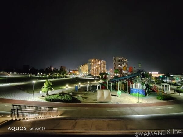 Nighttime cityscape with illuminated buildings and a colorful playground/ride area in the foreground.